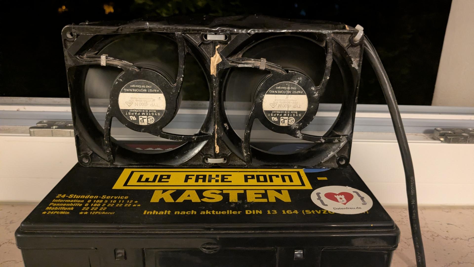 Two old Papst-Fans connected together with cableties, sitting on a little Case with a „We Fake Porn“-Sticker on the window sill of my bedroom.