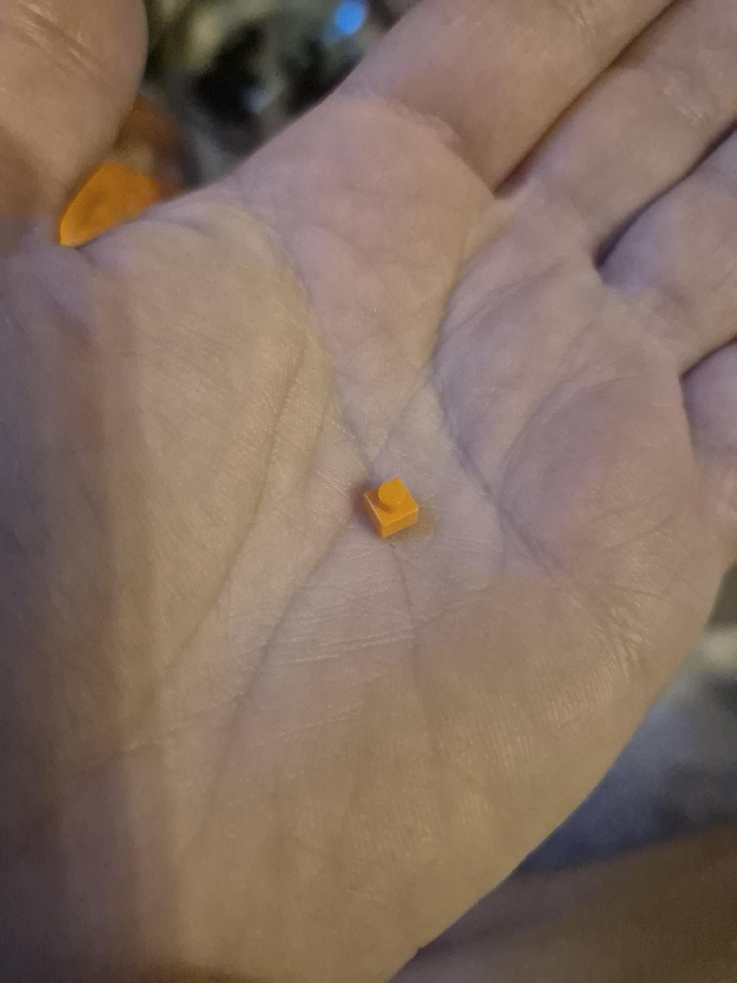Auf einer Hand liegt ein winziger orangener Klemmbaustein mit nur einer Noppe.