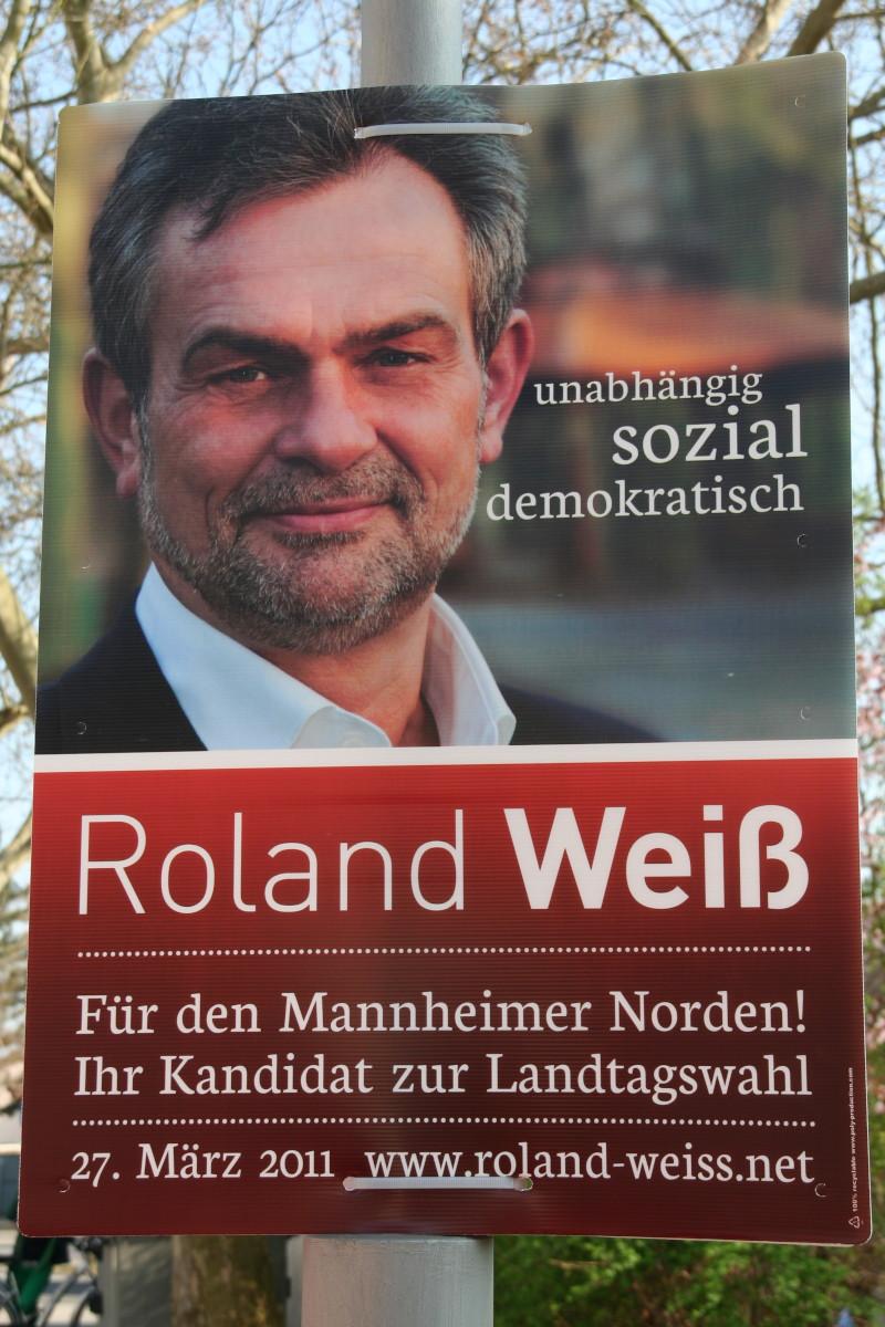 Foto im Hochformat. Wahlplakat eines Herrn namens Roland Weiß. Sein Slogan ist „unabhängig, sozial, demokratisch“. Er bewirbt sich „für den Mannheimer Norden! Ihr Kandidat zur Landtagswahl. 27. März 2011, www.roland-weiss.net“.